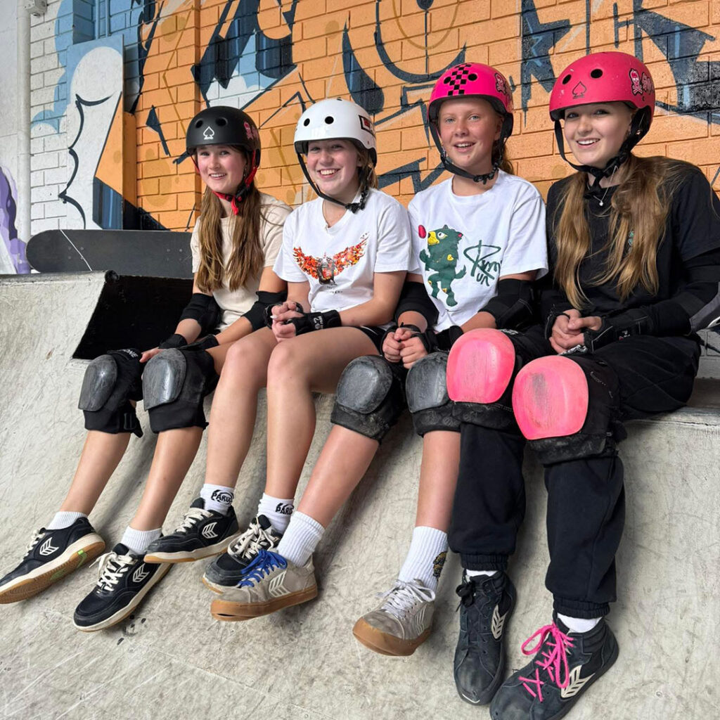 Girls wearing helmets and pads during a skateboard coaching session in Tasmania